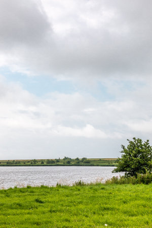 Green flat meadows near the river and the cloudy sky