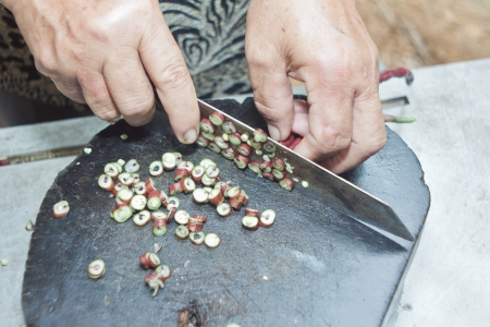 The hand is cutting cow pea to small pieces by knife on chopping block.の写真素材