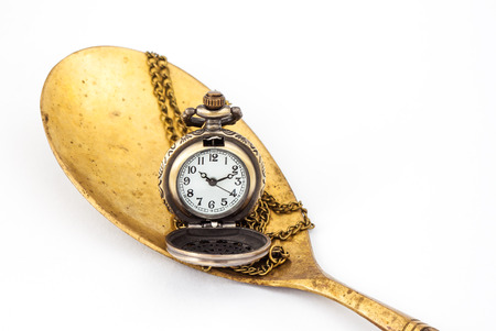 Small watch with chain on brass ladle with white backgroundの写真素材