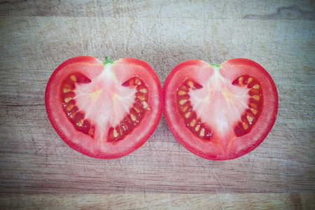 Half cut of red tomato in heart shape on wooden plankの写真素材