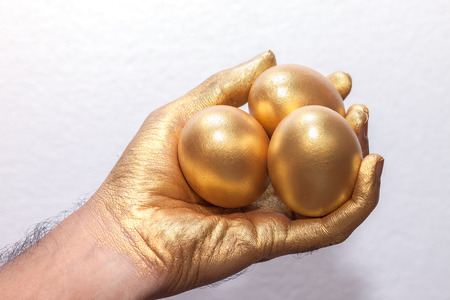 Golden egg on golden hand on whiteの写真素材