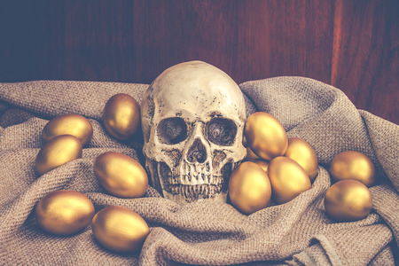Human skull surrounded by golden easter egg on brown sack with dark brown wooden backgoundの写真素材