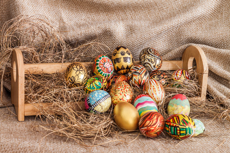 Colorful painted easter egg on hay in wooden shelf with sack backgroundの写真素材
