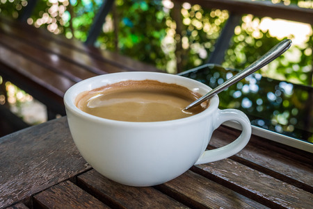 Cup of coffee on wooden table and green bokeh backgroundの写真素材