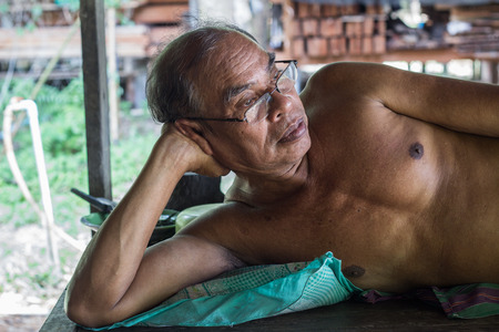 Thai aged man wearin eye glasses, wearing no shirt lying on bedの写真素材