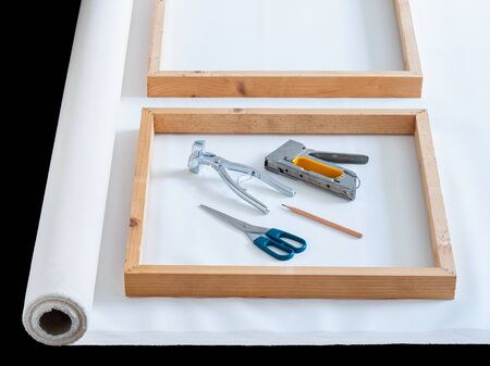 Closeup wooden frame on roll white artist cotton canvas with tool prepare for stretching on black background.の写真素材