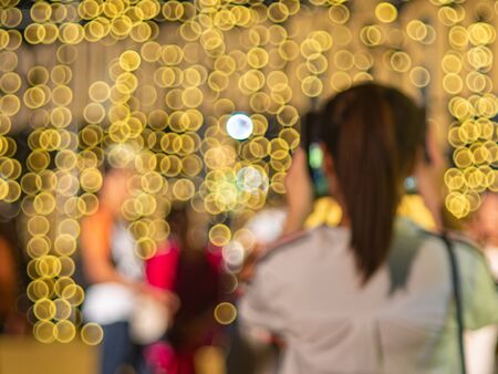 Defocus of unidentifield woman take a photo with blurry yellow light bulb hang like a wall on backgroundの写真素材