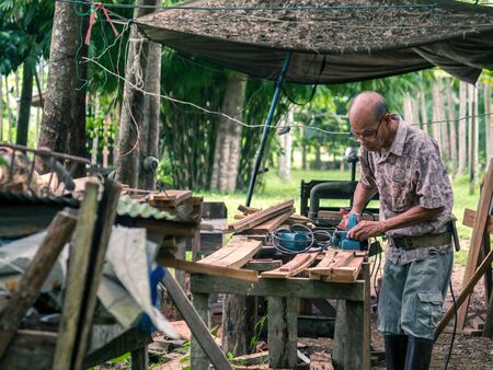 An Asian carpenter shaping wood with electric planer with green tree in blackground.の写真素材