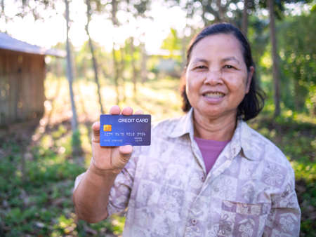 Smiling asian senoir woman showing credit card in rubber plantation, Thailandの写真素材