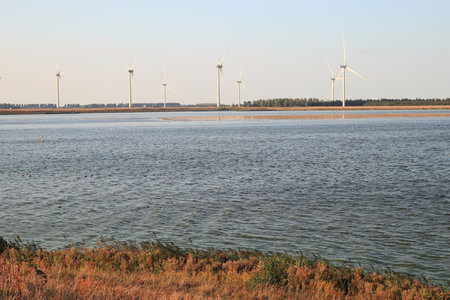 Several wind turbines generating electricity, blue sky in the background and the North Sea in the...