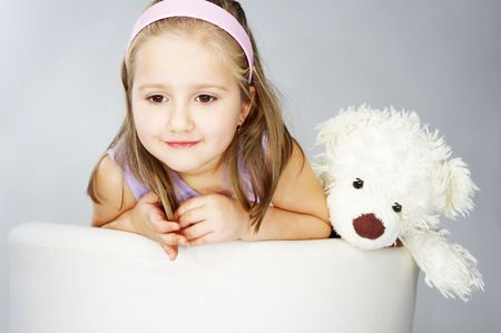 Nice young girl in pink on light background sitting on white chair with teddy bearの写真素材