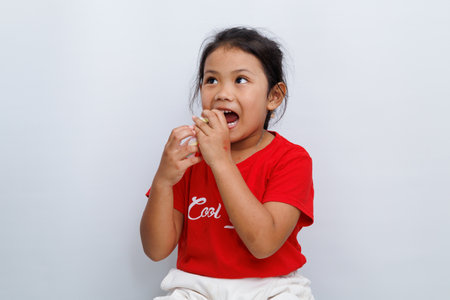 A small Asian girl wearing a red t-shirt is biting a strawberry with an expression of curiosity about the taste of the strawberry.の写真素材