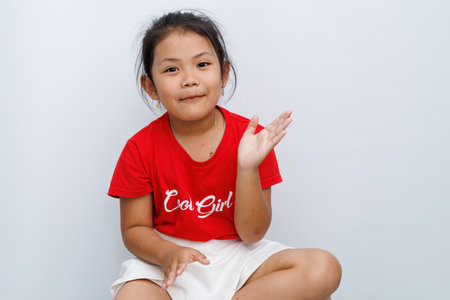 little asian girl with red t-shirt shows a gesture of clapping her hands together with her hands still in the air. smiling showing a happy expression. isolated on white background.の写真素材