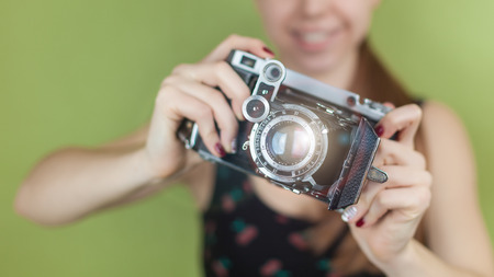 smiling girl with vintage  retro camera taking photo on green background