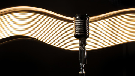 Vintage retro microphone on the black background with light waveの写真素材