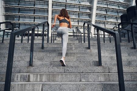 Young athletic woman running upstairs, training at urban city stadium