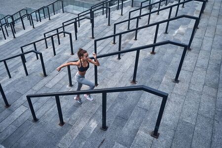 Top view of young athletic woman running upstairs fast, training at urban city stadium