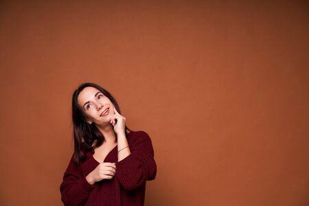 Young happy and positive woman thinking holding her finger on face on brown background