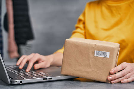 Woman sending parcel using her laptop. Working from homeの写真素材
