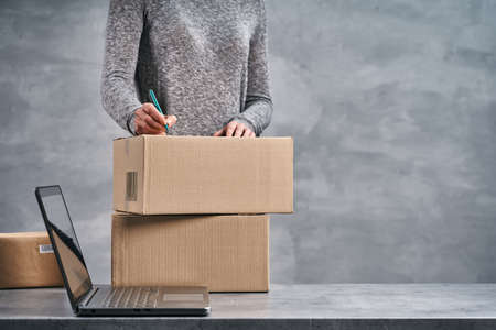 Woman writing addresses on the boxes, preparing parcels for send. Working from home