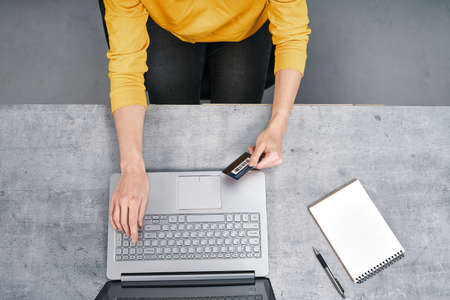 Shot from above of woman working with laptop and holding bank card in handの写真素材
