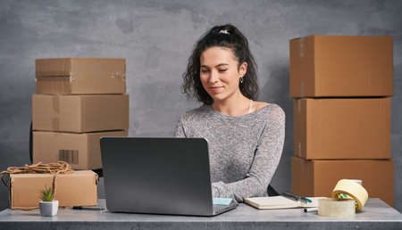 Business woman working from home with laptop and notepad, preparing boxes with products for deliveryの写真素材