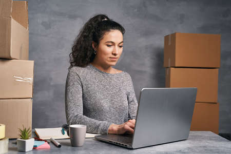 Business woman working from home with laptop and notepad, preparing boxes with products for deliveryの写真素材