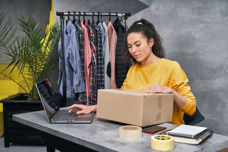 Woman sending parcel using her laptop. Working from homeの写真素材