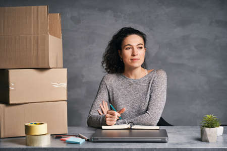 Business woman working from home with laptop and notepad, preparing boxes with products for deliveryの写真素材