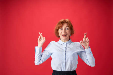 Beautiful redhead woman crossing her fingers with emotional face on red backgroundの写真素材