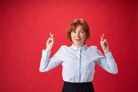 Beautiful redhead woman crossing her fingers on red backgroundの写真素材