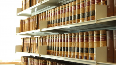 Shelves laden with colourful ornate antique gilt tooled leather bound books in a library angled away...