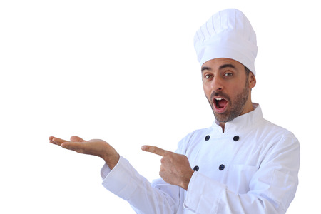 Handsome young male chef or baker in his white toque and uniform pointing to his empty outstretched hand with the palm up for product placement with copyspace, isolated on whiteの写真素材