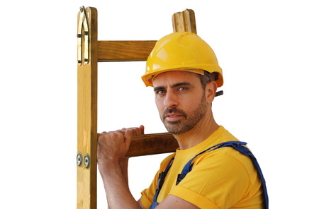 Handsome young bearded workman in a yellow hardhat and matching t-shirt carrying a wooden ladder isolated on whiteの写真素材