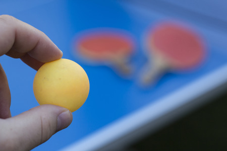 Close up of hand holding yellow ball with table tennis rackets in the background