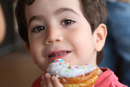 Young boy eating donut with white creamの写真素材