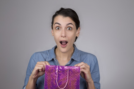 Attractive young woman with surprised expression on her face as she open gift bagの写真素材