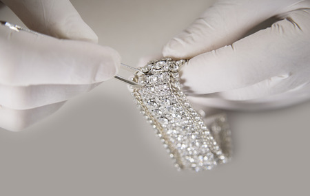Close up Man Hand with White Gloves Putting Diamond on a Bracelet Jewellery Using Tweezers on a White Backgroundの写真素材