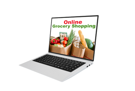 Online grocery shopping using a laptop concept with an open laptop screen showing text and brown paper packets filled with healthy fresh vegetables and a baguette isolated on whiteの写真素材