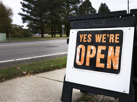 Yes we're open sign placed on a pavement near the road. Signs to encourage potential customers to shop at the store are spread alongsmall towns.の写真素材