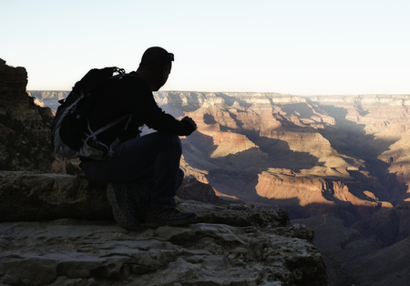 silhouette of a man sitting on the south rim of the Grand Canyon out looking The Viewの写真素材
