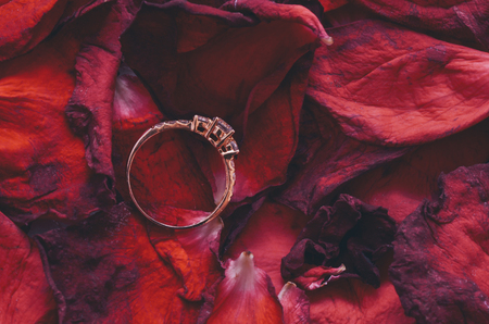 close up photo of a wedding ring on a red flower petal (selective focus)の写真素材
