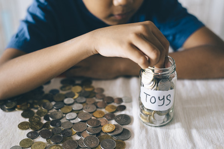 young asian boy putting coins into glass jar. Saving money to buy toys. Saving conceptの写真素材