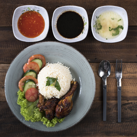 Popular Malaysian dish Nasi Ayam or chicken rice with baked chicken pieces, tomato, cucumber, salad, soup, soy sauce and chili sauce.の写真素材