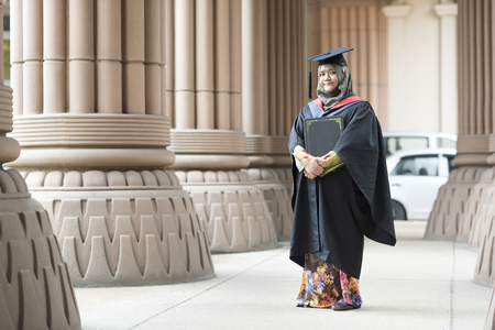 education concept - young woman holding a degree certificate while smiling on her graduation dayの写真素材