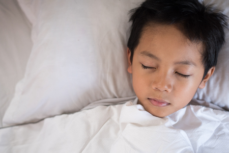 boy sleeping on bed with white sheet and pillow.asian kid fall asleep daydreaming.sleep conceptの写真素材