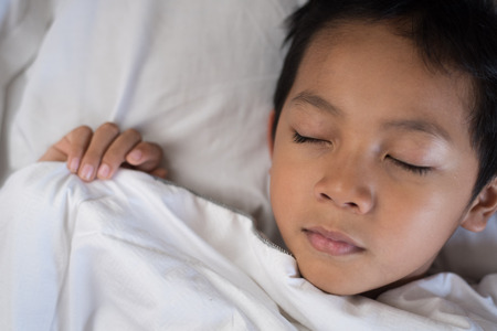 boy sleeping on bed with white sheet and pillow.asian kid fall asleep daydreaming.sleep conceptの写真素材
