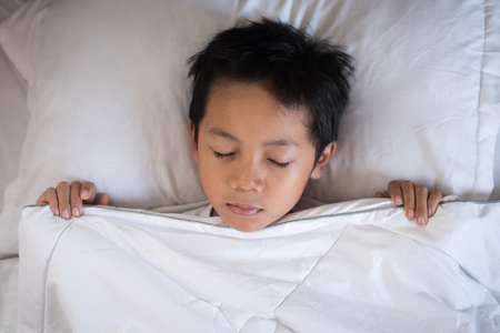 boy sleeping on bed with white sheet and pillow.asian kid fall asleep daydreaming.sleep conceptの写真素材