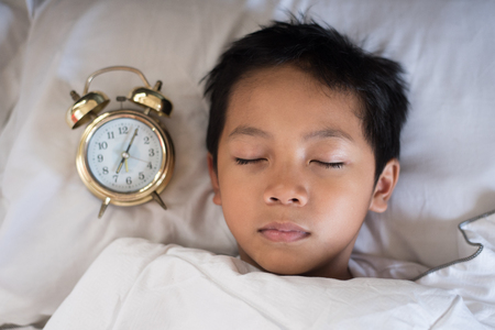 young boy sleeping with alarm clock on the bed at the morning.asian boy fall asleep.sleep conceptの写真素材