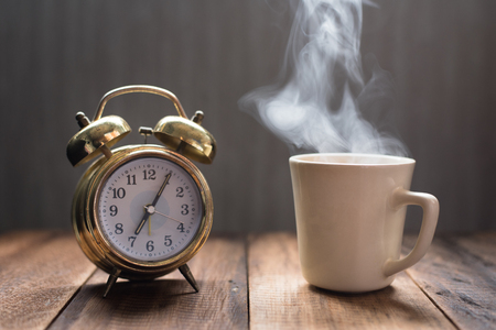hot tea / coffee and golden alarm clock on a wooden table - it's tea time conceptの写真素材
